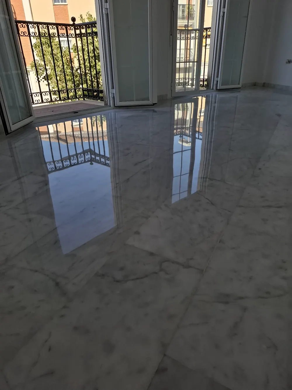 Mármol blanco pulido espejo reflejando balcones — trabajo real de Pulimentos Jiménez